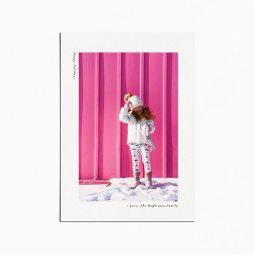 holiday card with an image of a little girl standing in the snow in front of a pink wall