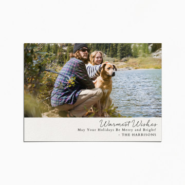 Holiday card with an image of a couple and their dog who are in a forest and crouched by a river. the title reads "Warmest Wishes"