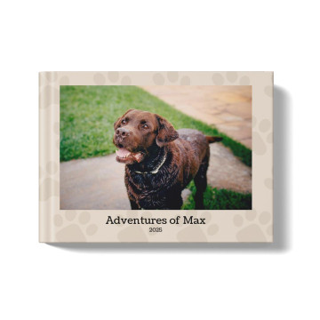 Pets photobook with beige background and paw-print pattern. At the center of the book is a photo of a brown labrador retriever and the title beneath it says: Adventures of Max, 2025"