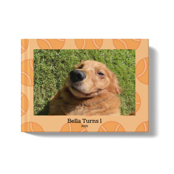 Pets Photobook with an orange background and tennis ball pattern. At the center of the cover is an image of a golden retriever lying in the grass, with a title beneath the image that says: "Bella Turns 1, 2025"