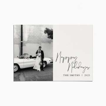 Holiday card with a black and white image of a married couple standing in front of a white convertible car. the title reads "Happy Holidays"