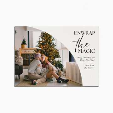 Holiday Card with an image of a couple embracing as they sit in a living room in front of a Christmas tree. The title reads "Unwrap the Magic"