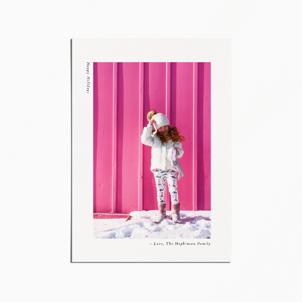 holiday card with an image of a little girl standing in the snow in front of a pink wall