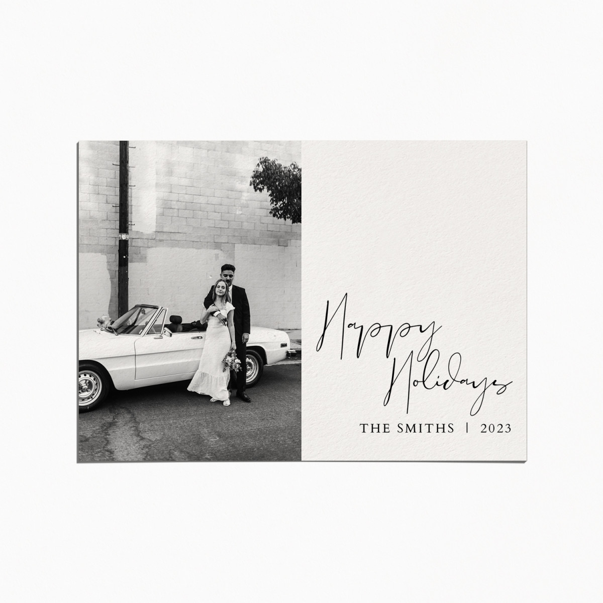 Holiday card with a black and white image of a married couple standing in front of a white convertible car. the title reads "Happy Holidays"