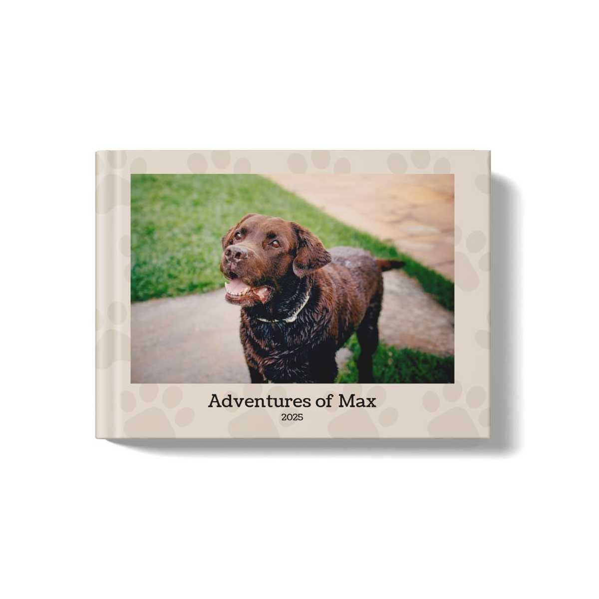 Pets photobook with beige background and paw-print pattern. At the center of the book is a photo of a brown labrador retriever and the title beneath it says: Adventures of Max, 2025"