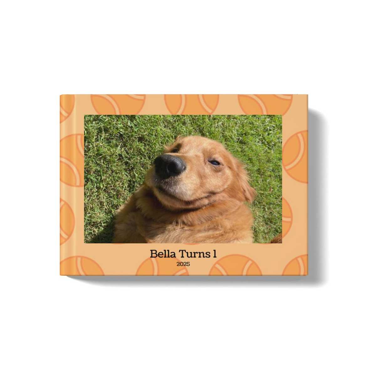 Pets Photobook with an orange background and tennis ball pattern. At the center of the cover is an image of a golden retriever lying in the grass, with a title beneath the image that says: "Bella Turns 1, 2025"