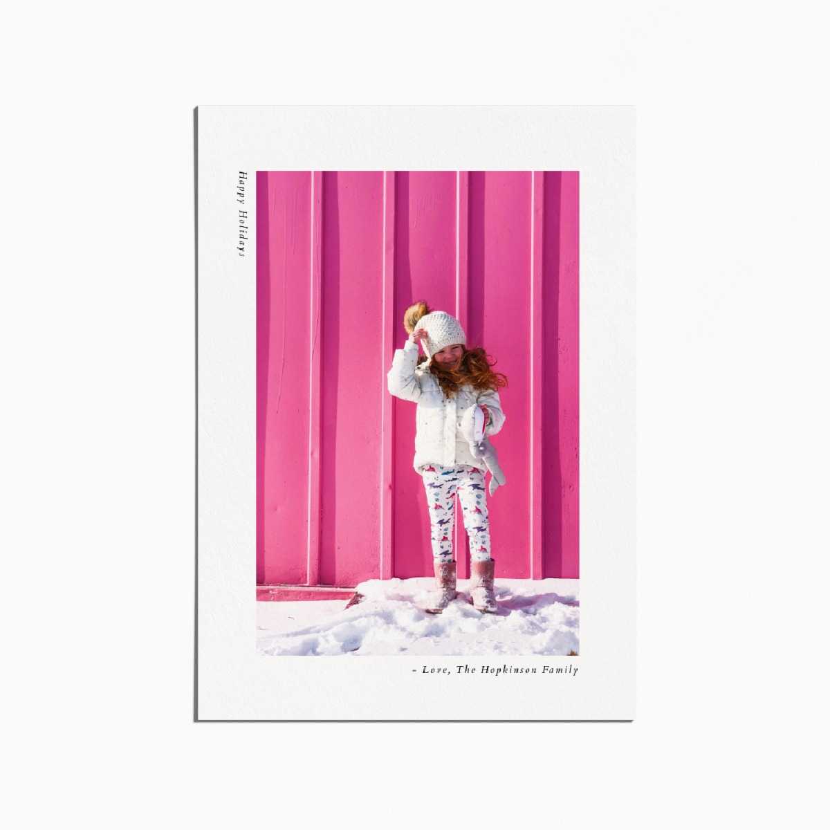 holiday card with an image of a little girl standing in the snow in front of a pink wall